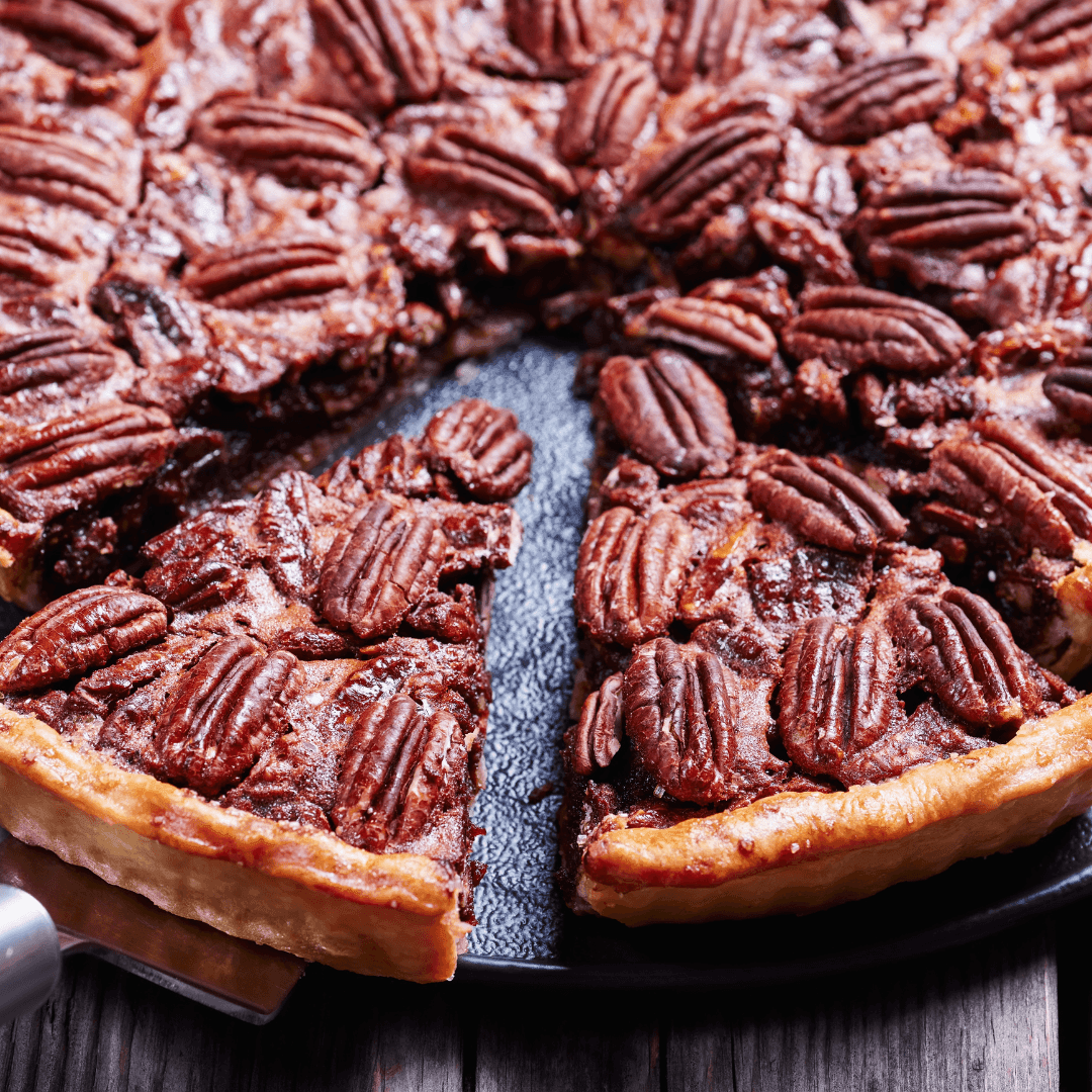 Close-up of a pecan pie with one slice being served on a spatula.